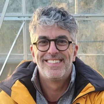 Portrait de Lorenzo, souriant, devant la serre de son potager.